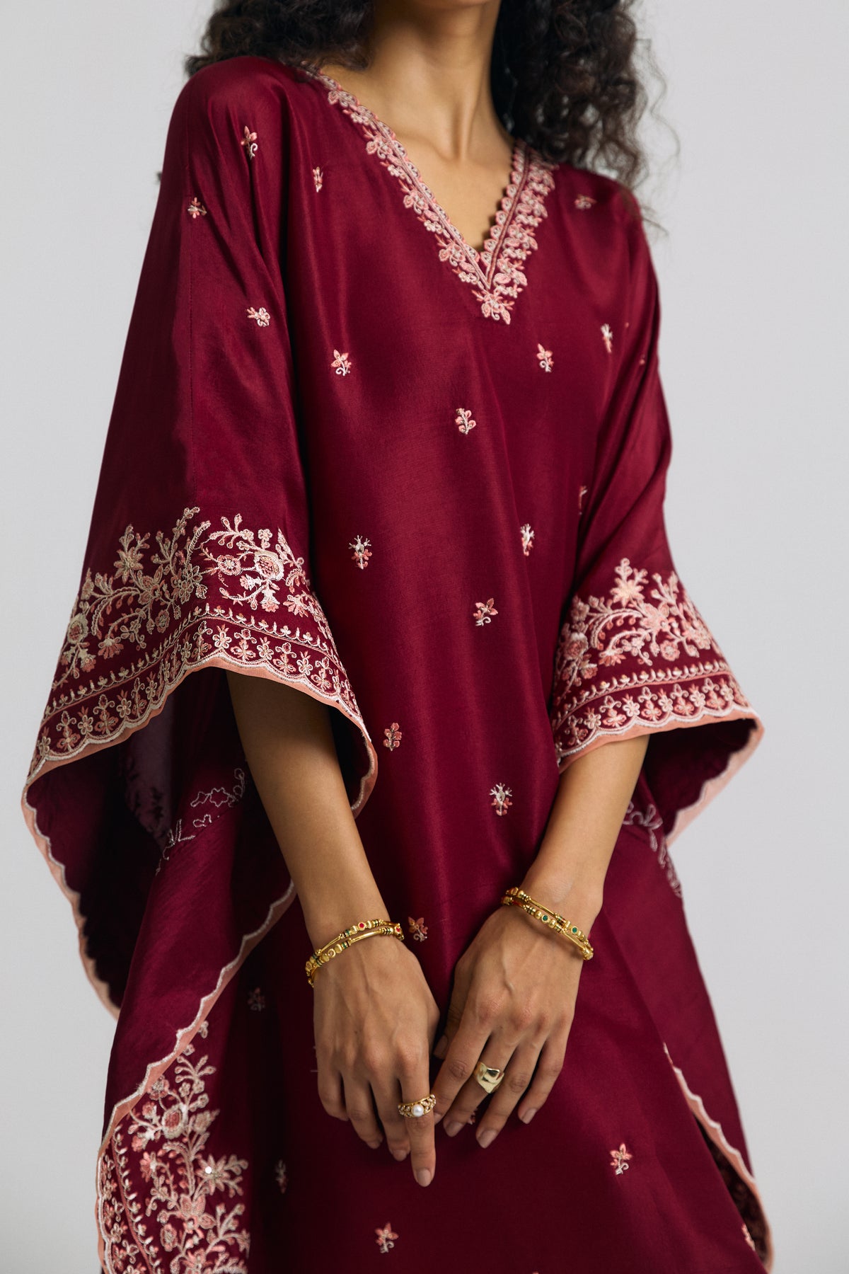 Close-up of petal-edged V-neckline with adda embroidery and peach accents on a burgundy silk kaftan dress