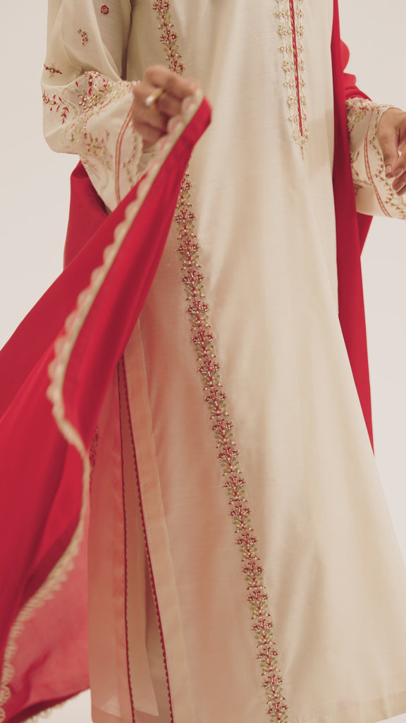 The White and Red Set by Mannam is a three-panelled pure silk kurta with a collared neckline, hand embellishments tracing the neckline, sleeves and panel seams, deep red accents throughout, lace edging and organza sleeve detail. It comes with straight-cut silk trousers featuring cutwork and petal-edged embroidery at the hem, and a pure silk deep red dupatta.